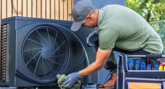 A technician in work attire cleans an outdoor air conditioning unit near a wooden wall. Tools are organized beside him for efficient service.